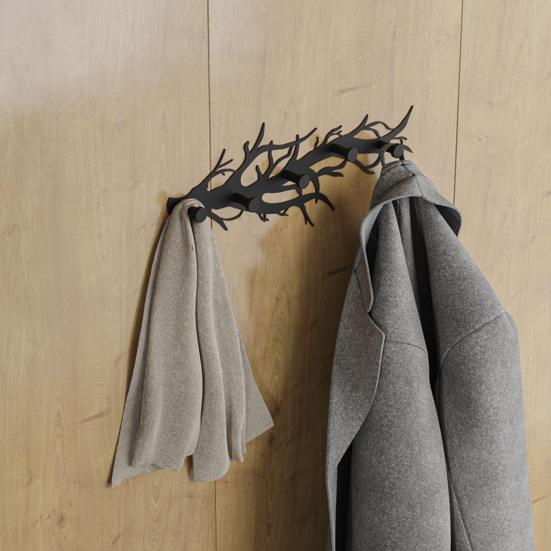 Μία μεταλλική κρεμάστρα μαύρη σε σχήμα κλαδιού τοποθετημένη σε ξύλινο τοίχο με κρεμασμένα ένα γκρι παλτό και ένα κασκόλ