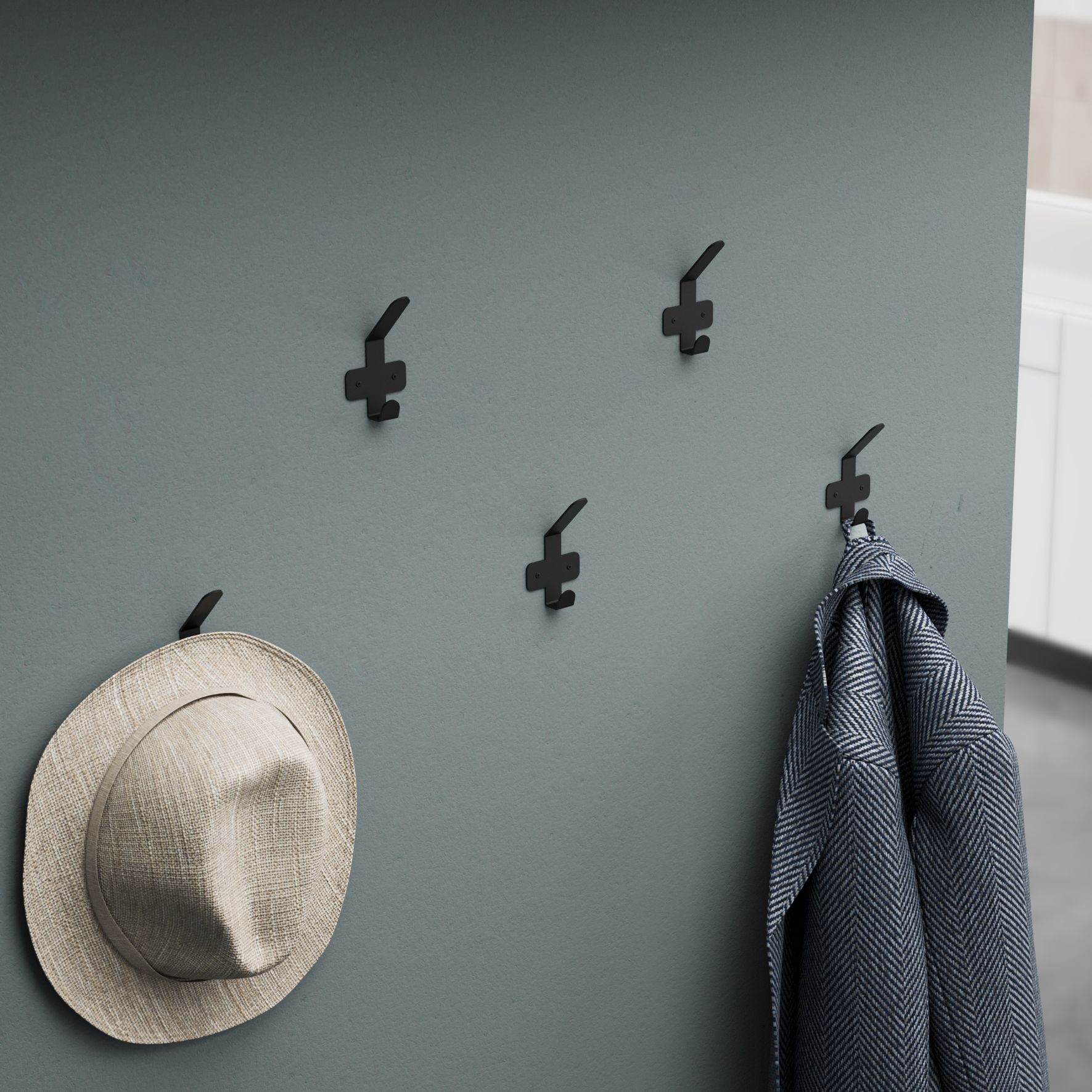 Μεταλλική μαύρη κρεμάστρα 1 θέσης τοποθετημένη σε γκρι τοίχο με κρεμασμένο ένα γκρι παλτό και ένα μπεζ καπέλο.